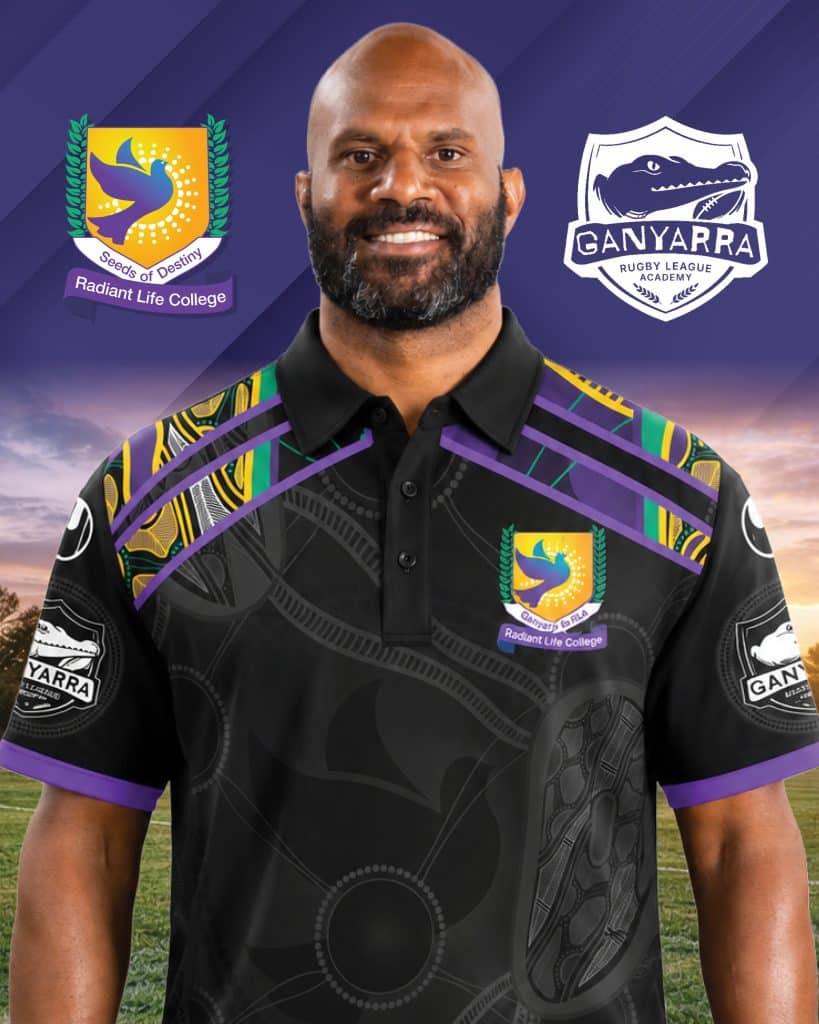 Smiling man in a patterned black shirt with college and rugby academy logos on a purple backdrop behind him