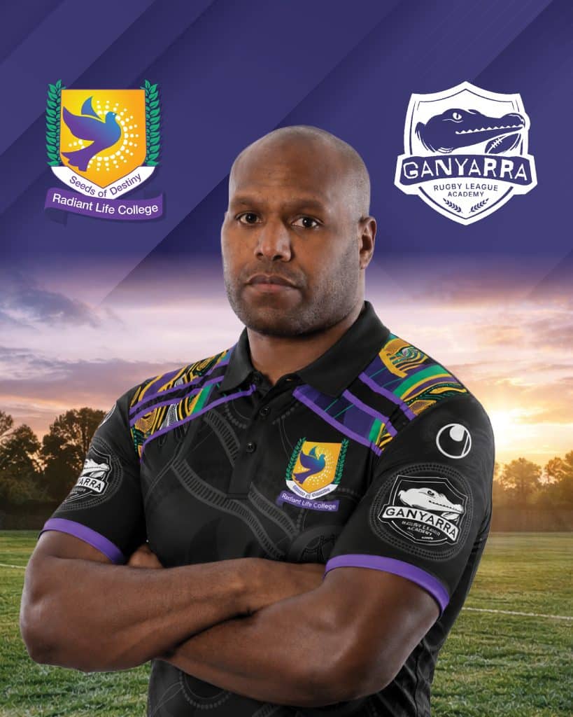 Portrait of a rugby player wearing a black jersey with purple and green accents arms crossed logos on chest and sleeve sunset field behind him