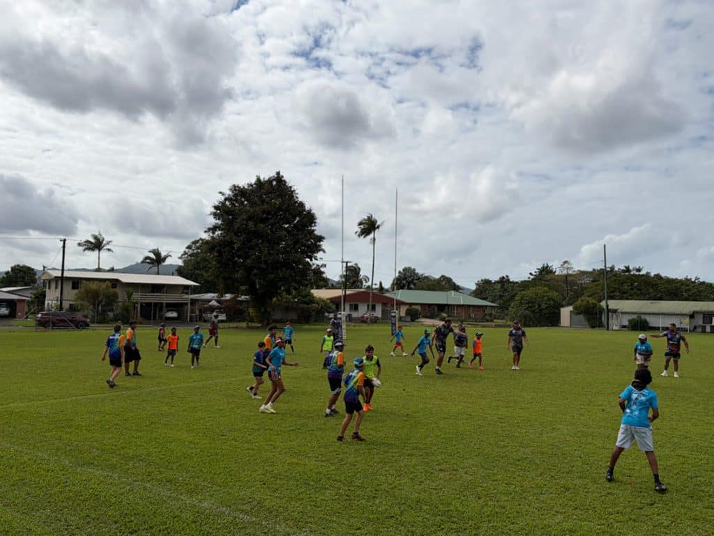 Group of children playing a team sport on a grassy field wearing colorful bibs under a cloudy sky
